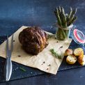 roast shoulder shoulder of lamb on a piece of parchment with roast potatoes and asparagus.
