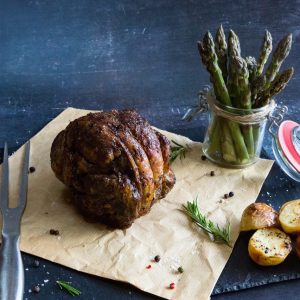 shoulder of lamb on a piece of parchment with roast potatoes and asparagus.