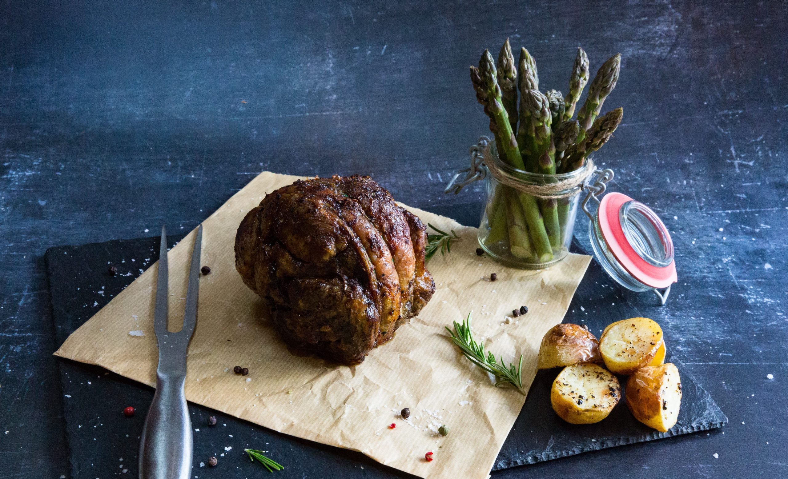 roast shoulder shoulder of lamb on a piece of parchment with roast potatoes and asparagus.