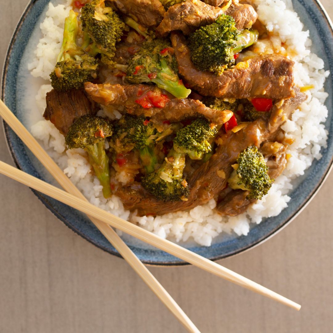 a plate of beef and broccoli with rice and chop sticks sitting on top