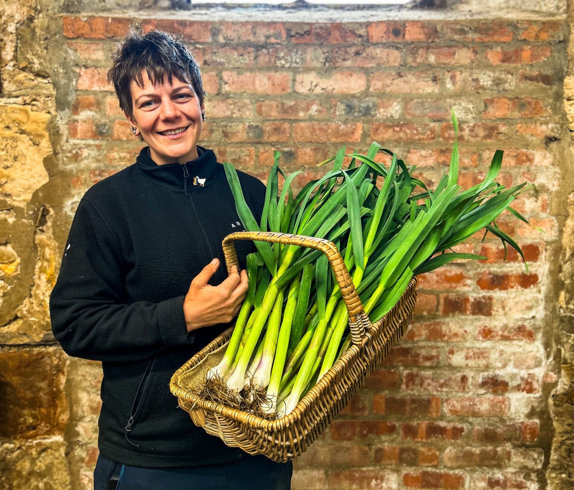 person standing holding a basket of green garlic
