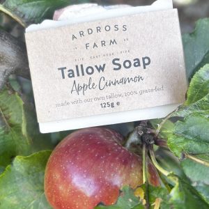 picture of a bar of tallow soap resting on a branch with a red apple underneath