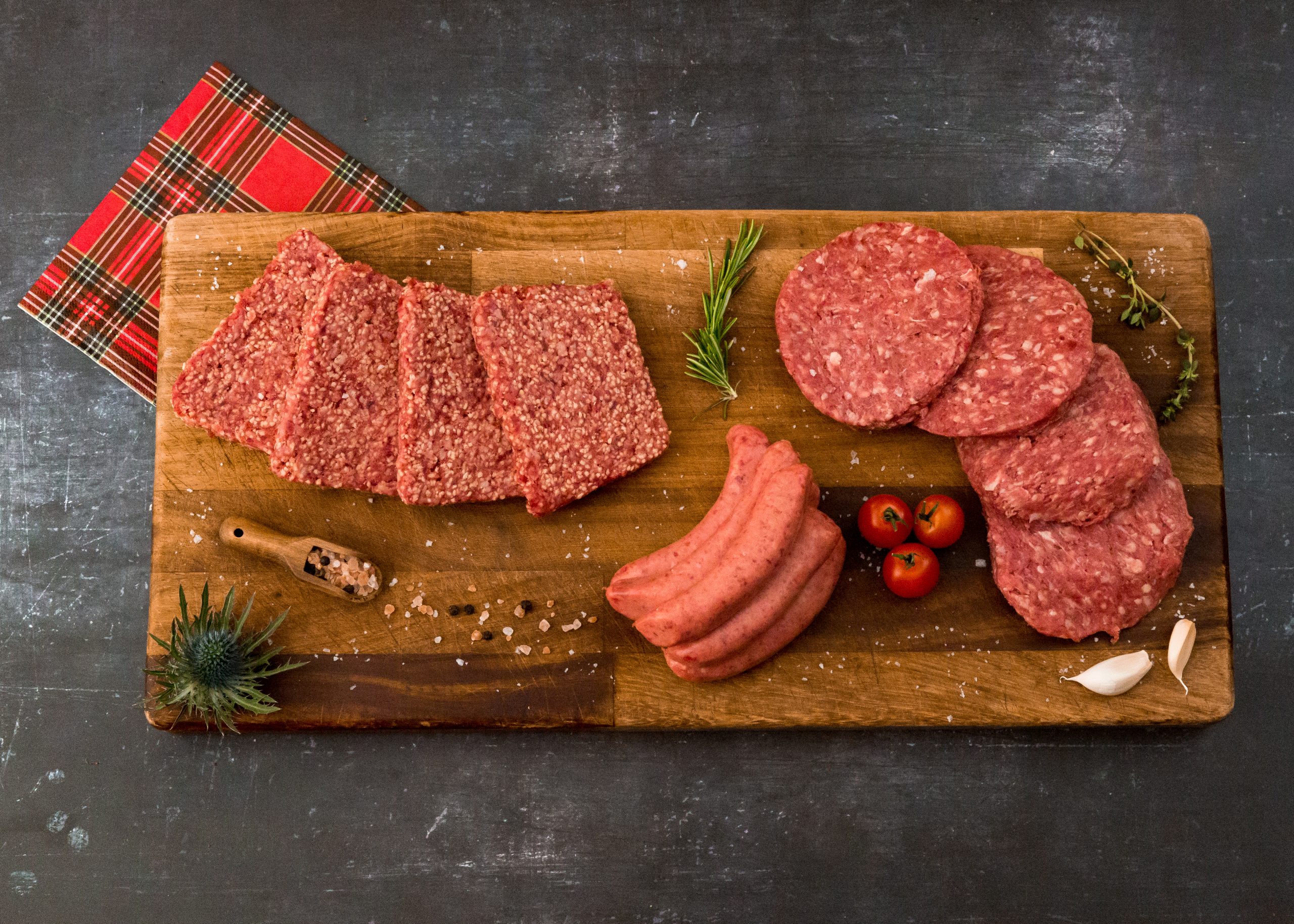 steak sausages, beef burgers and lorne sausages on a wooden chopping board with a tartan napkin