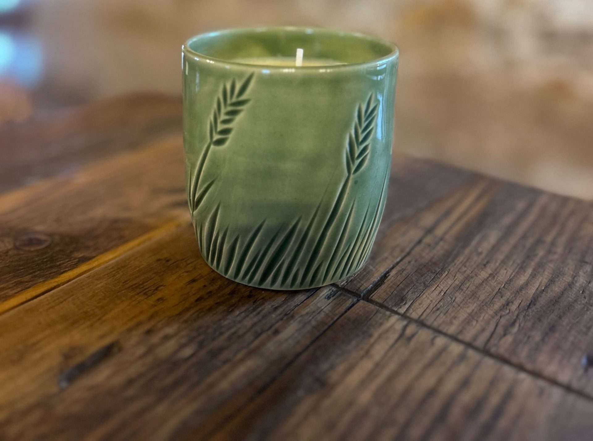 green ceramic candle with wheat patterns sitting on wooden table.
