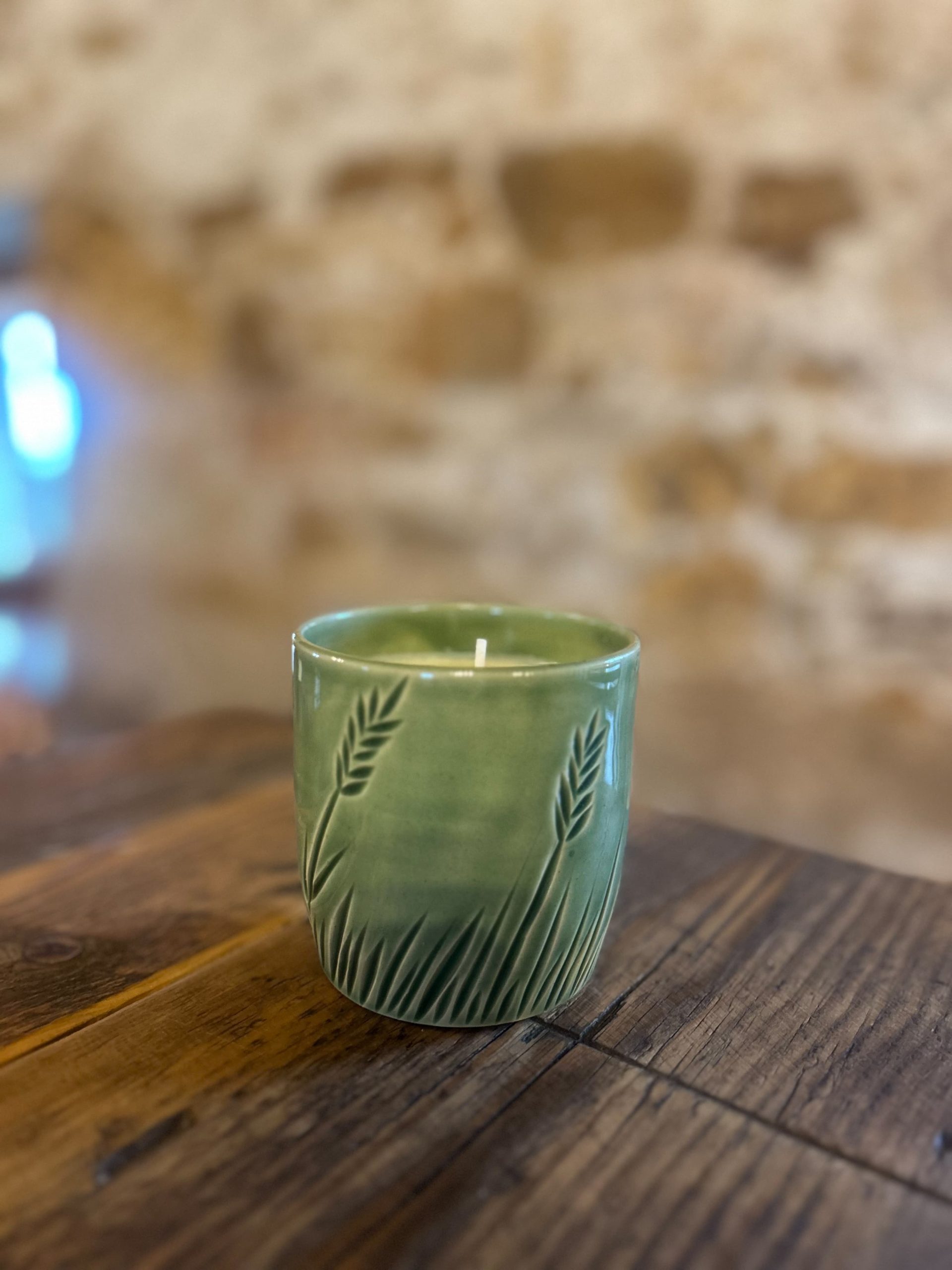 green ceramic candle with wheat patterns sitting on wooden table.
